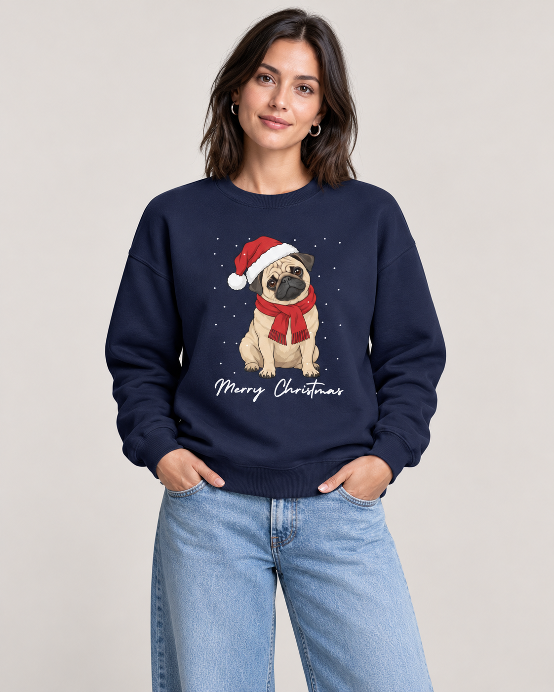 A woman wearing a navy blue crewneck sweatshirt with a Christmas pug graphic, paired with light blue jeans, against a solid light gray background.