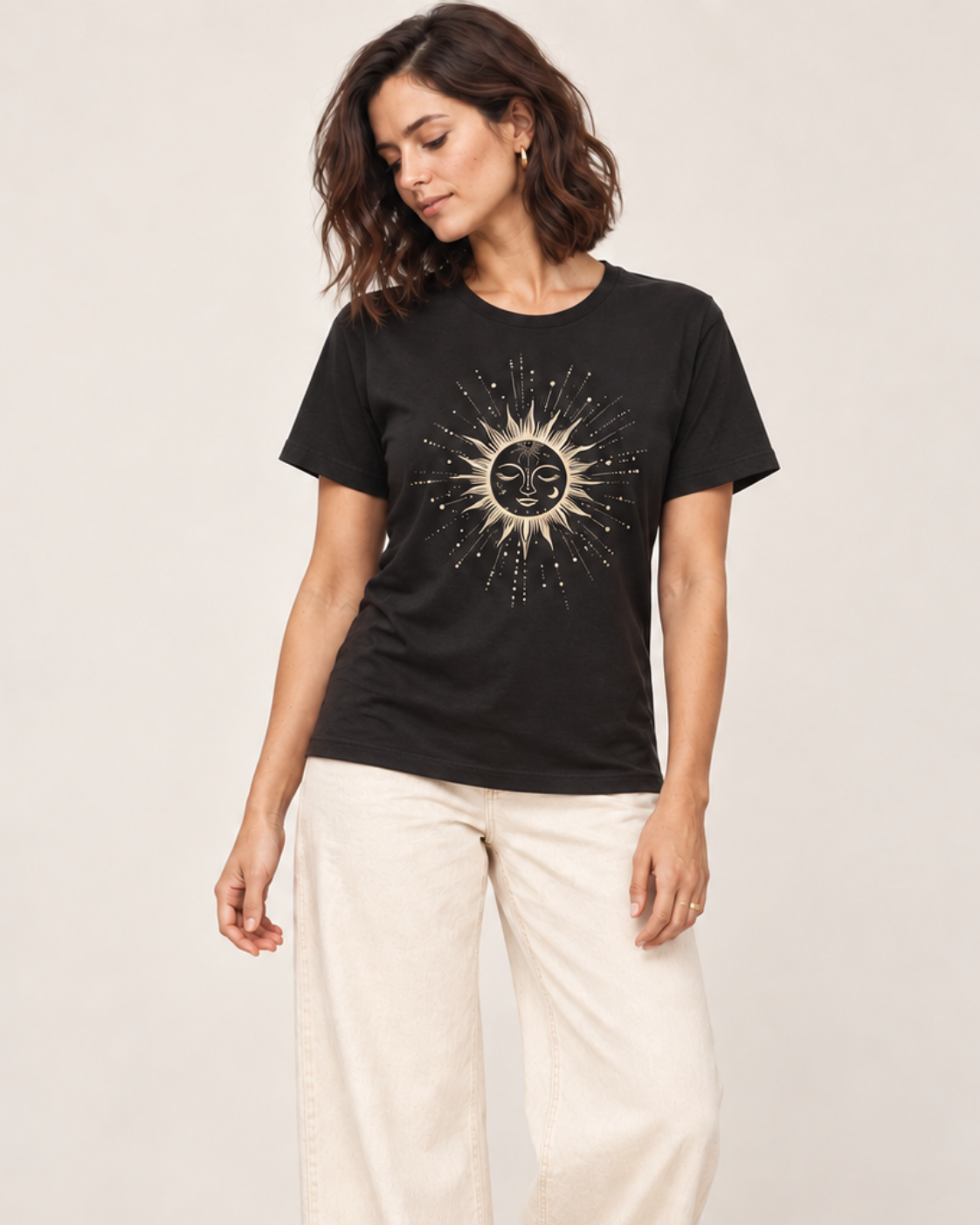 Woman wearing a black t-shirt featuring a celestial sun and moon with stone wide-leg trousers in a bright studio.