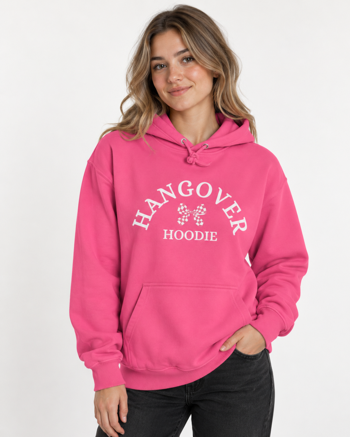 Woman wearing a candy-floss pink Hangover Hoodie featuring a white gingham bow design with black jeans in a bright studio.