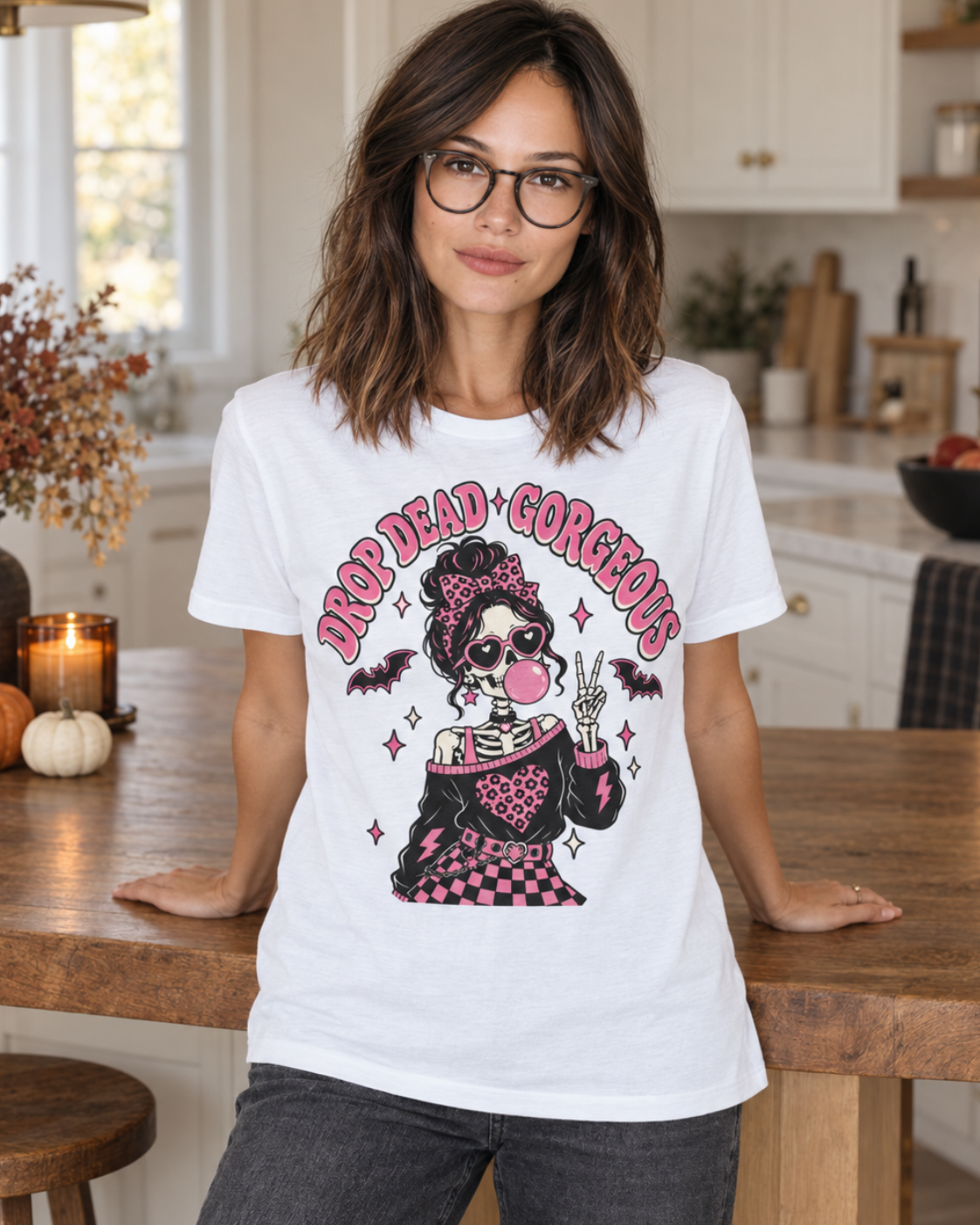 Woman wearing a white Drop Dead Gorgeous skeleton Halloween T-shirt in a warm autumn kitchen.