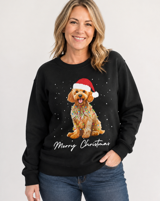 A woman wearing a black crewneck sweatshirt with a festive Christmas graphic of a golden Cockapoo dog in a Santa hat and the text 'Merry Christmas' underneath, paired with blue jeans against a light grey background.