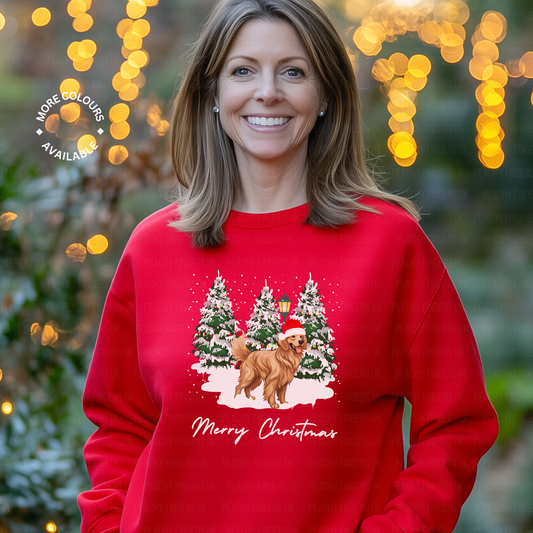 Woman wearing red Christmas sweatshirt with golden retriever in Santa hat design, standing in front of snowy pine trees and “Merry Christmas” text.
