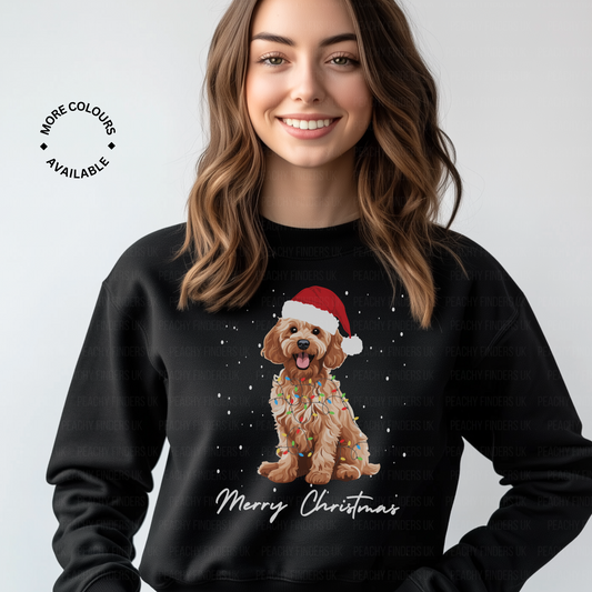 Woman wearing a black Christmas-themed sweatshirt with a golden cockapoo wearing a Santa hat, wrapped in fairy lights and 'Merry Christmas' text.