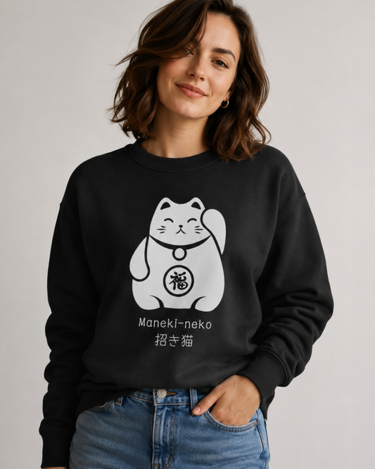 A woman wearing a black crewneck sweatshirt with a white Maneki-neko (lucky cat) graphic on the front, paired with blue jeans, against a plain light grey background.