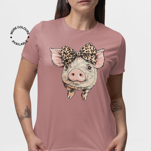 A woman with long brown hair wearing a mauve t-shirt with a graphic of a cute piglet wearing a leopard print bow.
