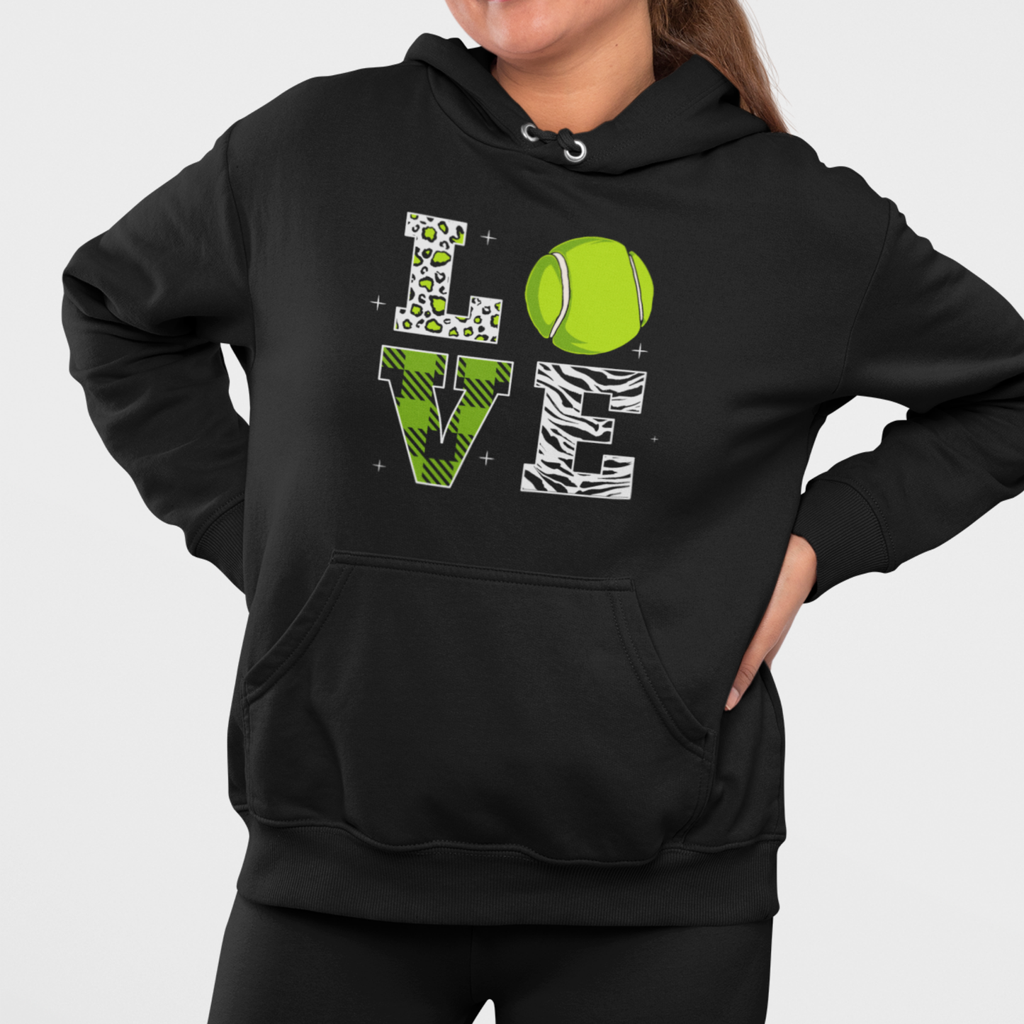 Woman wearing black tennis LOVE pullover hoodie with green animal print letters and tennis ball graphic, outdoor lifestyle photo