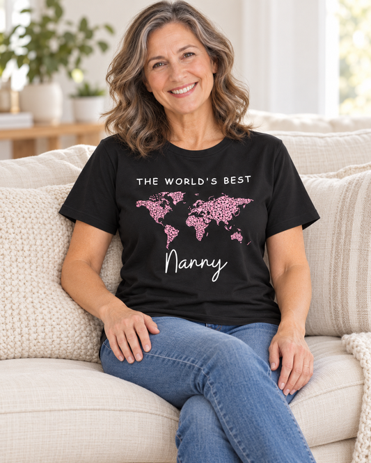 Woman sitting on a cream sofa wearing a black t-shirt with "The World's Best Nanny" printed in white text alongside a world map filled with small pink hearts
