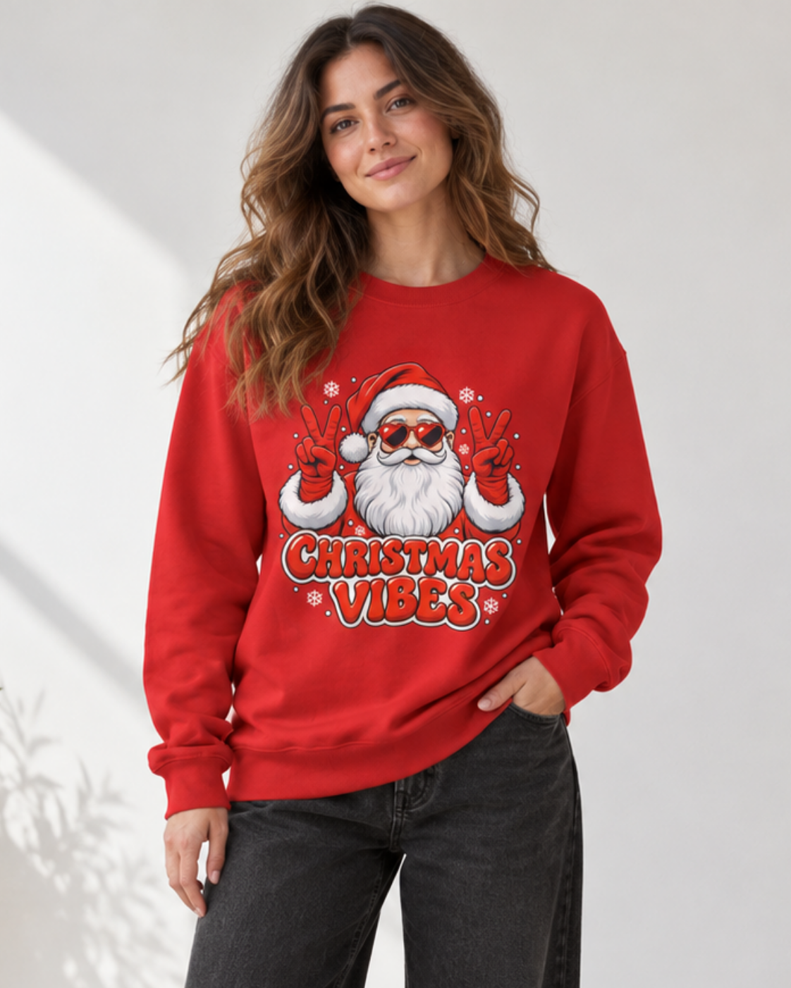 A woman wearing a red crewneck sweatshirt with a graphic of a Santa Claus wearing sunglasses and making peace signs above the text 'CHRISTMAS VIBES'.