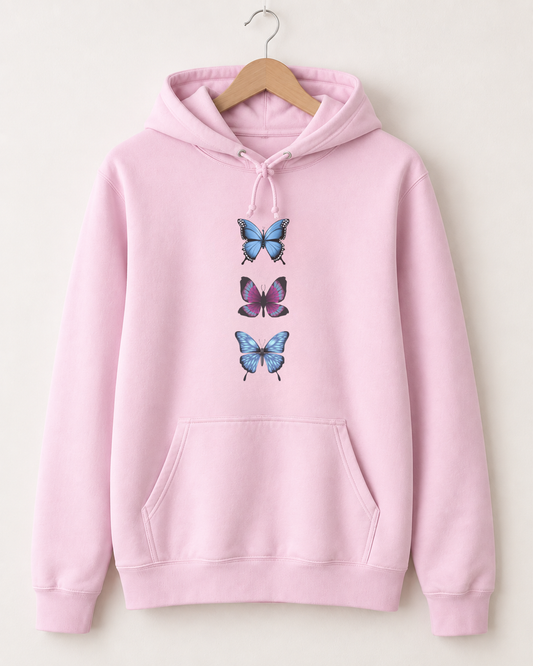 A light pink pullover hoodie hanging on a wooden hanger against a plain off-white background. The hoodie features a graphic print of three stacked butterflies on the center chest, with two blue butterflies and one purple butterfly.