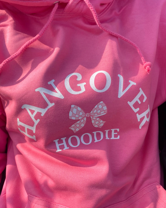 A pink hoodie with the text 'HANGOVER HOODIE' printed on the front, accompanied by a graphic of a checkered bow.
