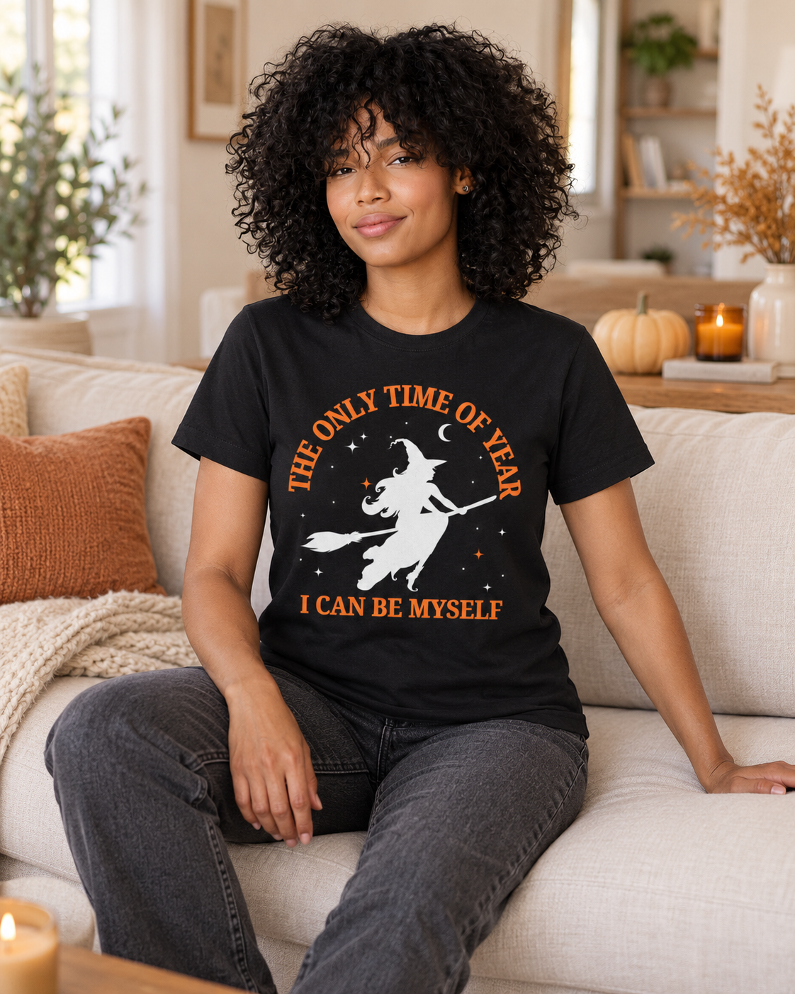 Black woman wearing a black witch Halloween T-shirt while relaxing on a cream sofa.