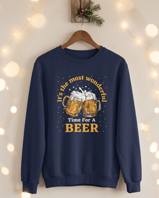 A navy blue crewneck sweatshirt featuring a festive graphic print with two clinking beer mugs, white foam, and the text 'It's the most wonderful Time For A BEER' in yellow and white lettering.