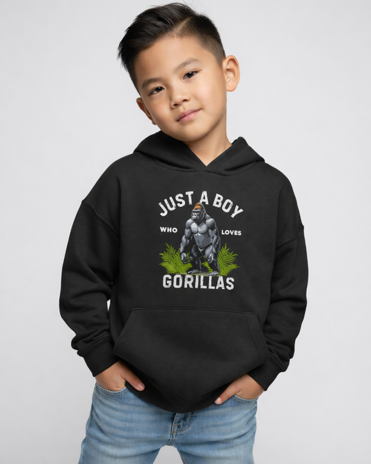 Young boy wearing a black “Just A Boy Who Loves Gorillas” hoodie standing with hands in pockets against a light grey studio background