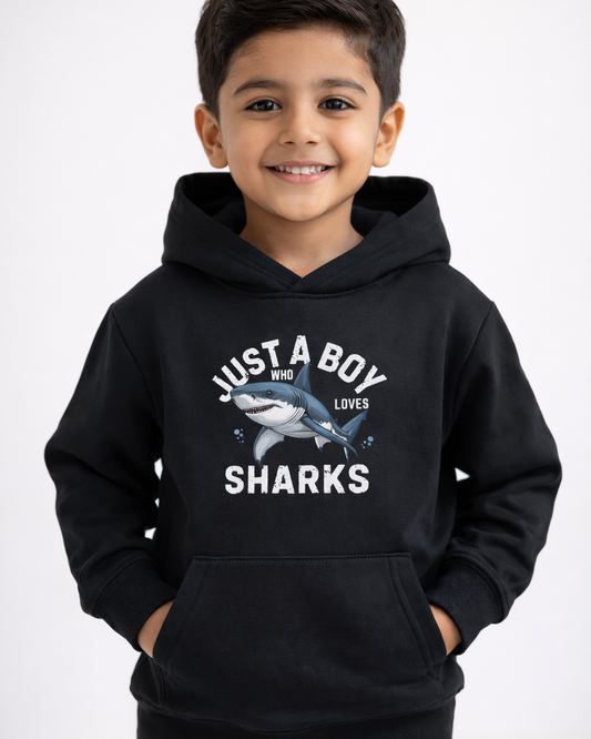 Boys black shark hoodie with “Just A Boy Who Loves Sharks” print, worn by smiling child in clean studio setting