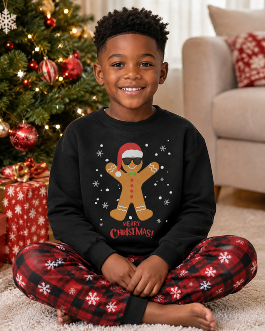 6-year-old boy wearing a black Christmas jumper featuring a gingerbread man with cool black sunglasses, Santa hat and snowflakes with festive pyjama bottoms, sitting cross-legged beside a decorated Christmas tree.