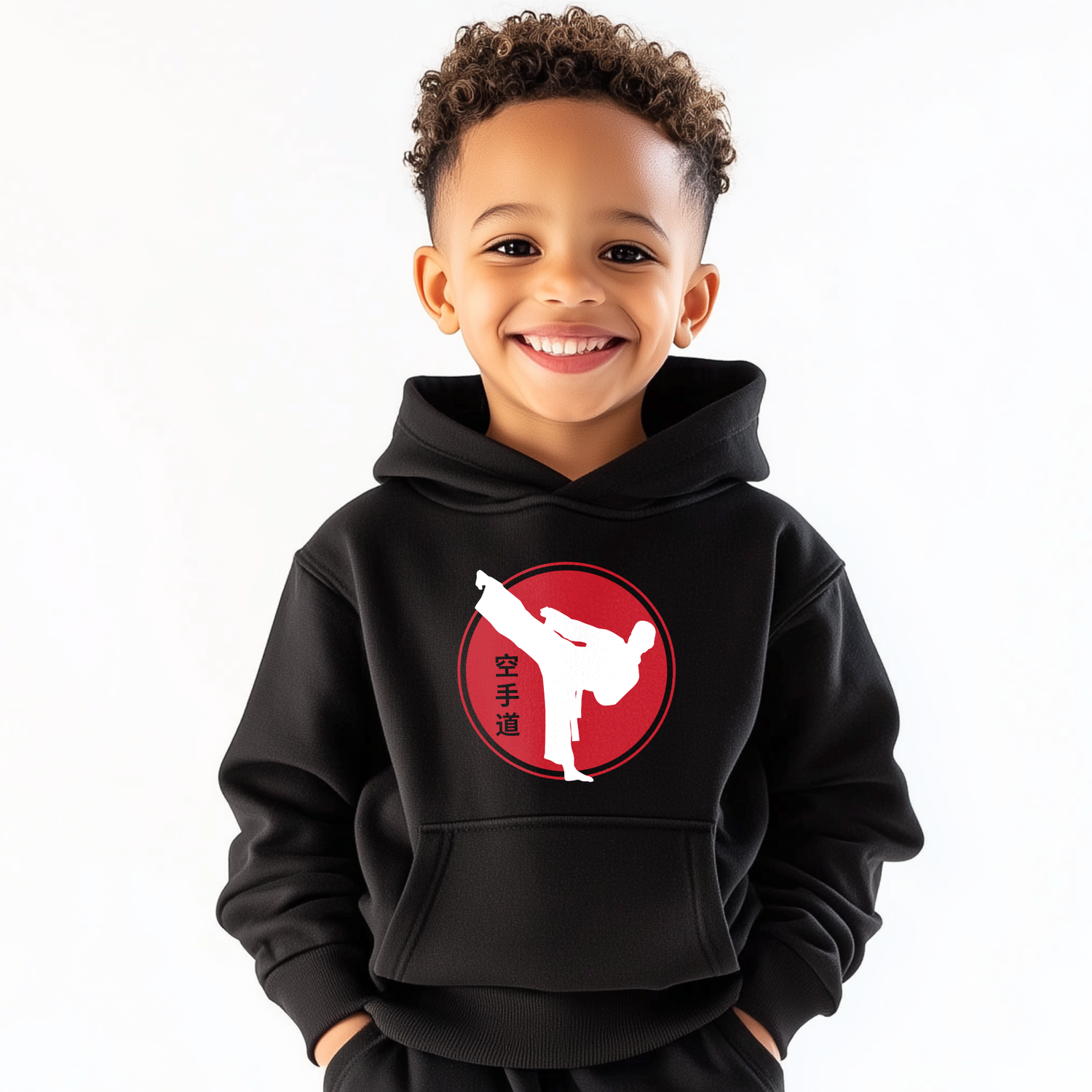 Young boy wearing a kids karate hoodie featuring a white kicking silhouette inside a red circle with Japanese kanji symbols, smiling against a plain white background.