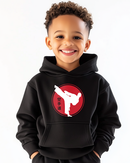 Young boy wearing a kids karate hoodie featuring a white kicking silhouette inside a red circle with Japanese kanji symbols, smiling against a plain white background.