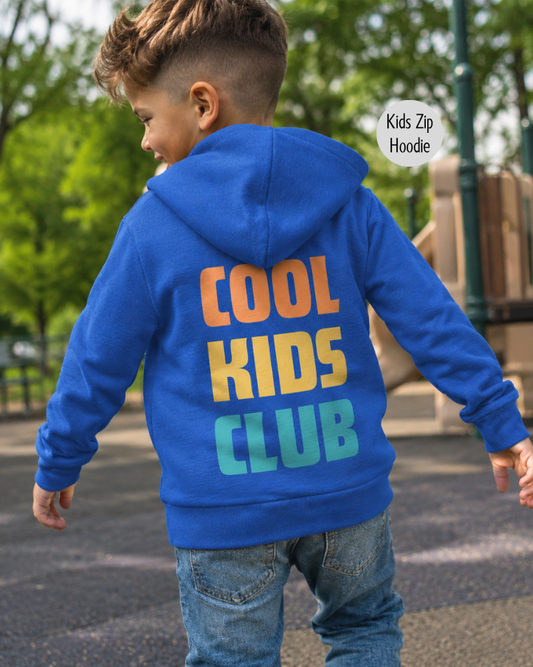 A child wearing a royal blue zip-up hoodie with 'COOL KIDS CLUB' printed in large gradient letters on the back, shown outdoors in a park setting.