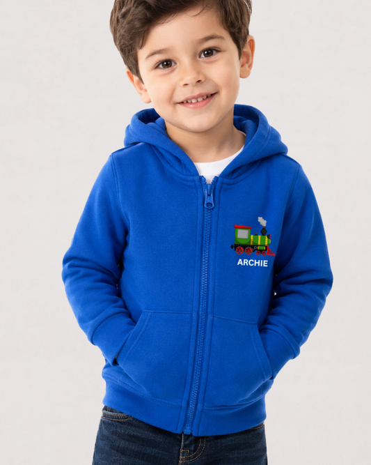 Young boy in a royal blue personalised steam train zip hoodie with name, hands in pockets, wearing jeans.