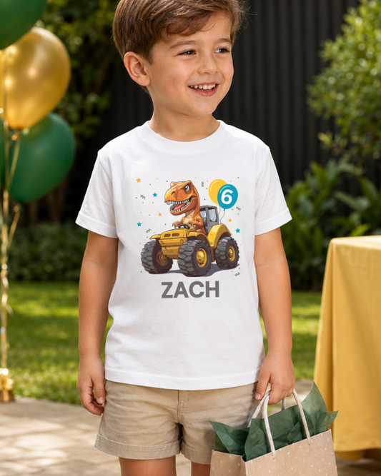 Personalised boys dinosaur tractor 6th birthday t-shirt worn at a garden party with green and gold balloons, gift bag and beige shorts.