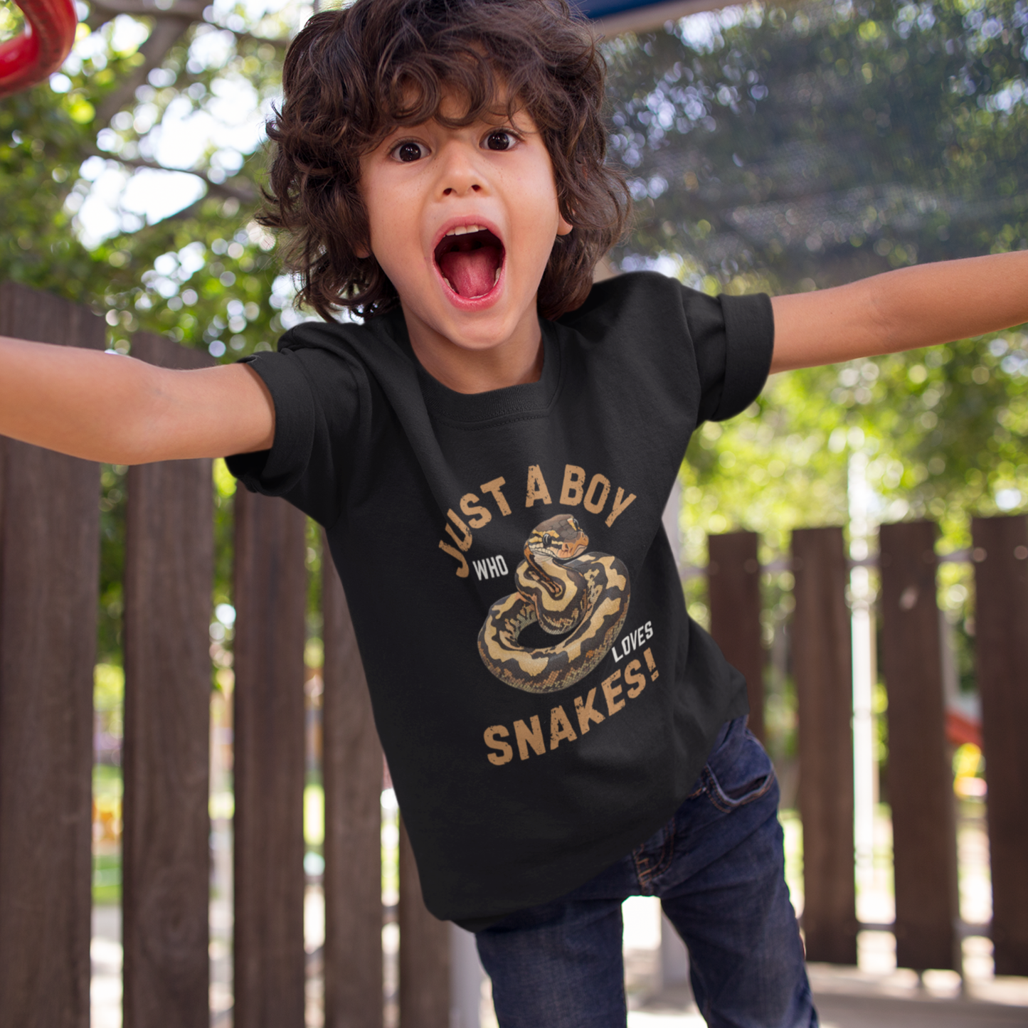 A boy at the park wearing a black cotton t-shirt featuring a ball python illustration with the slogan ‘Just a Boy Who Loves Snakes!’