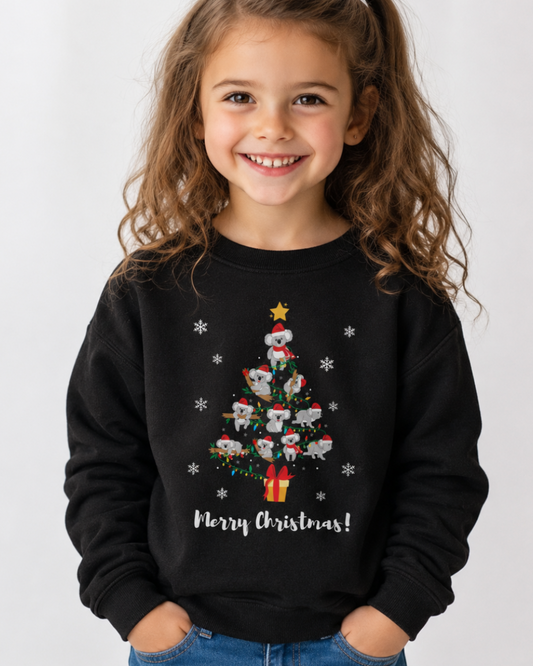 Smiling girl wearing a black Christmas sweatshirt featuring a Christmas tree made of koalas in Santa hats with fairy lights and snowflakes.