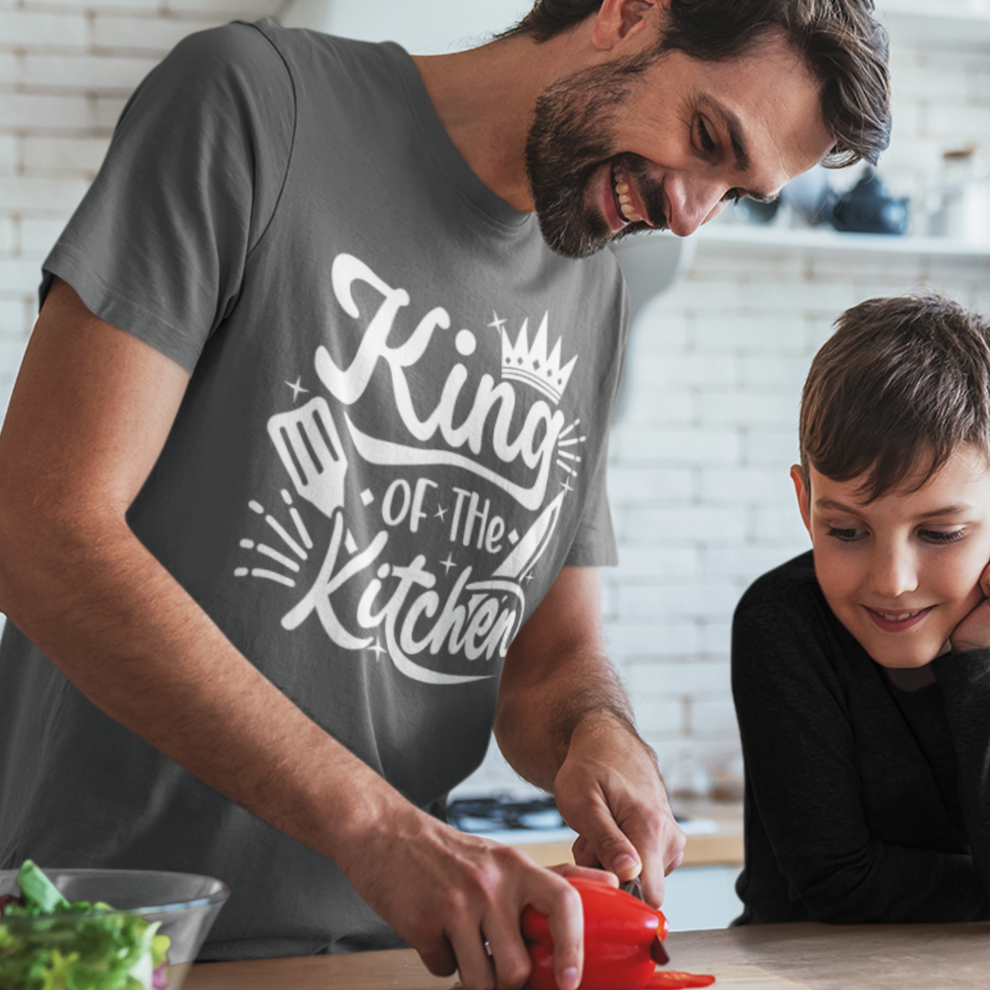 Man wears Dark Grey short sleeved cotton t-shirt with printed text 'King of the Kitchen' with crown, spatular, knife and stars