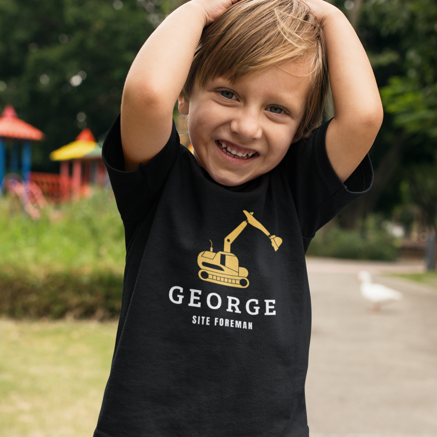 Smiling young boy wearing a black T-shirt with a yellow digger graphic and personalised name with “Site Foreman” text.