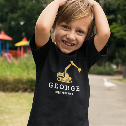 Smiling young boy wearing a black T-shirt with a yellow digger graphic and personalised name with “Site Foreman” text.