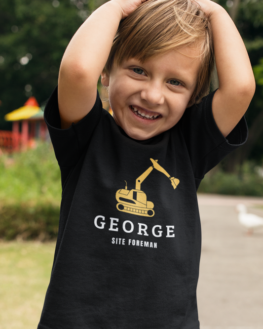 Smiling young boy wearing a black T-shirt with a yellow digger graphic and personalised name with “Site Foreman” text.
