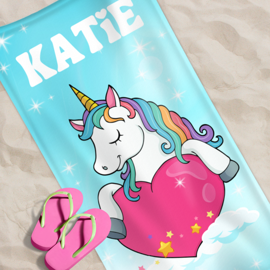 Girls custom name unicorn beach towel laying on the sand with pink flip flops on it