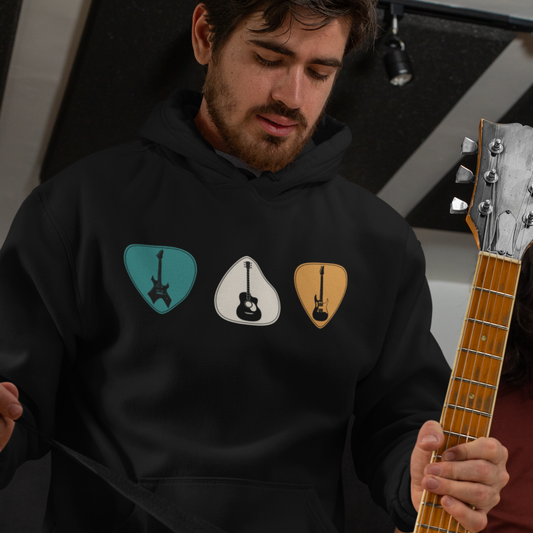A man wearing a black pullover hoodie with a vintage design of guitars and plectrums holding a real guitar.